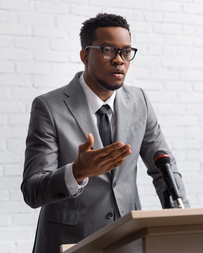 confident-african-american-business-speaker-on-tribune-with-microphone-in-conference-hall-e1661098107411.jpg